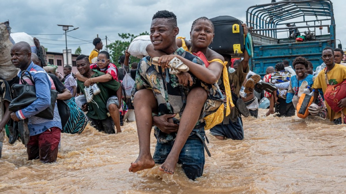 Morador carrega mulher enquanto outros avançam por enchente no bairro de Ndjili, em Kinshasa