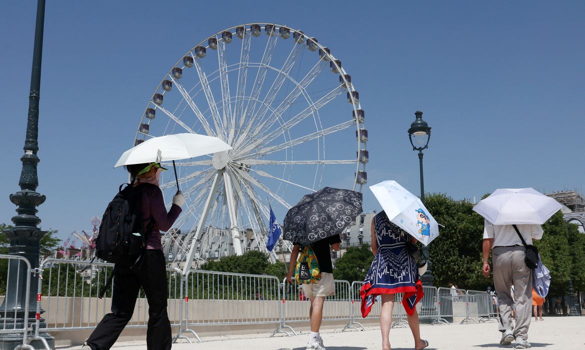 Turistas se protegem do sol com guarda-chuvas perto da roda-gigante do Jardim das Tulherias, em Paris, durante onda de calor, 2 de julho de 2025