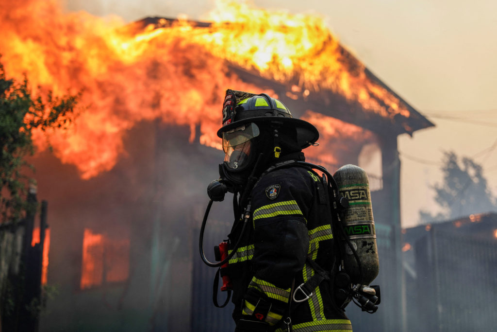 Bombeiro em frente a edifício em chamas durante incêndio florestal no Chile