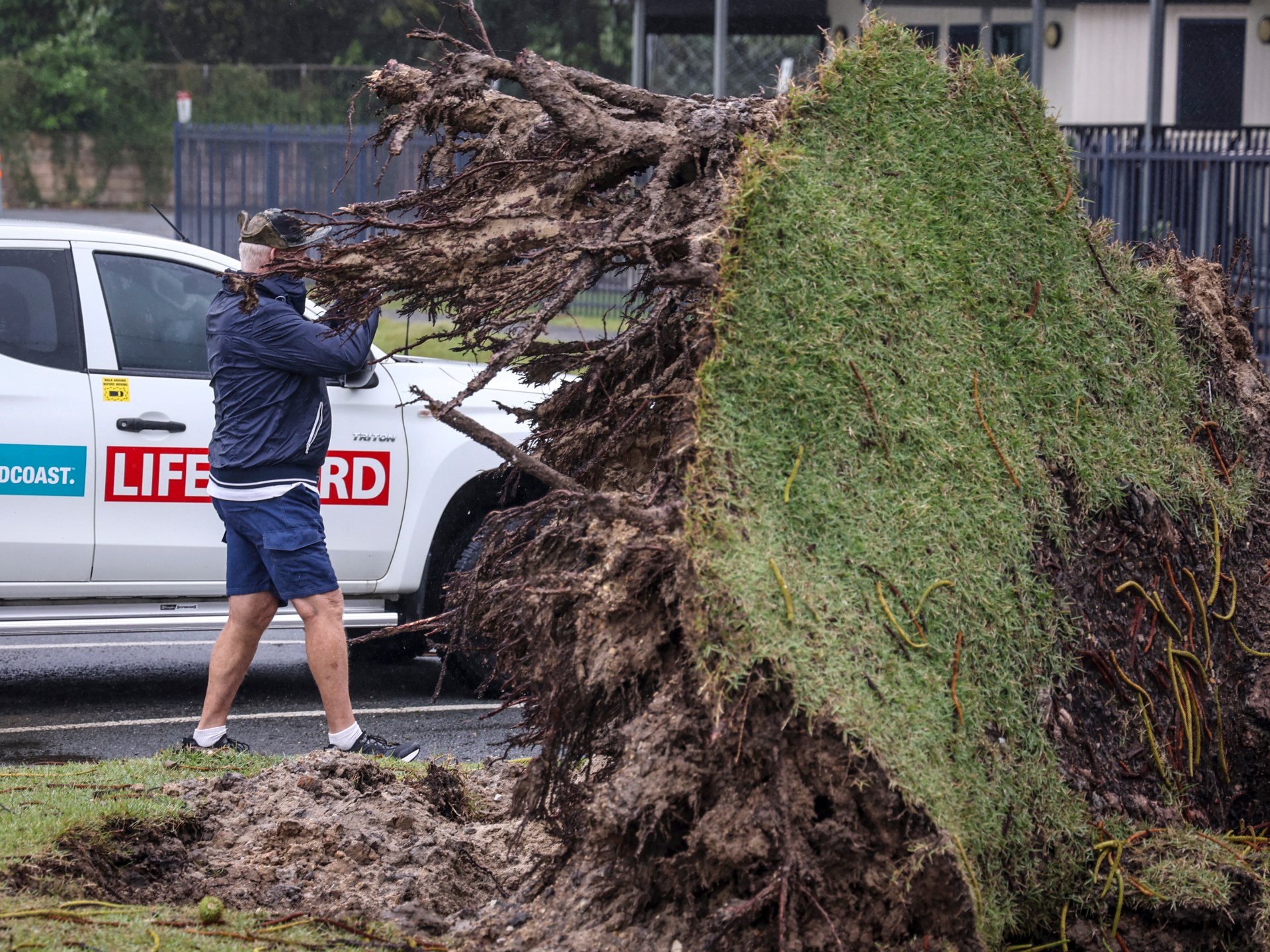 Homem observa árvore arrancada em frente ao Miami Beach Surf Lifesaving Club após o Ciclone Alfred na Gold Coast, Austrália, em 8 de março de 2025