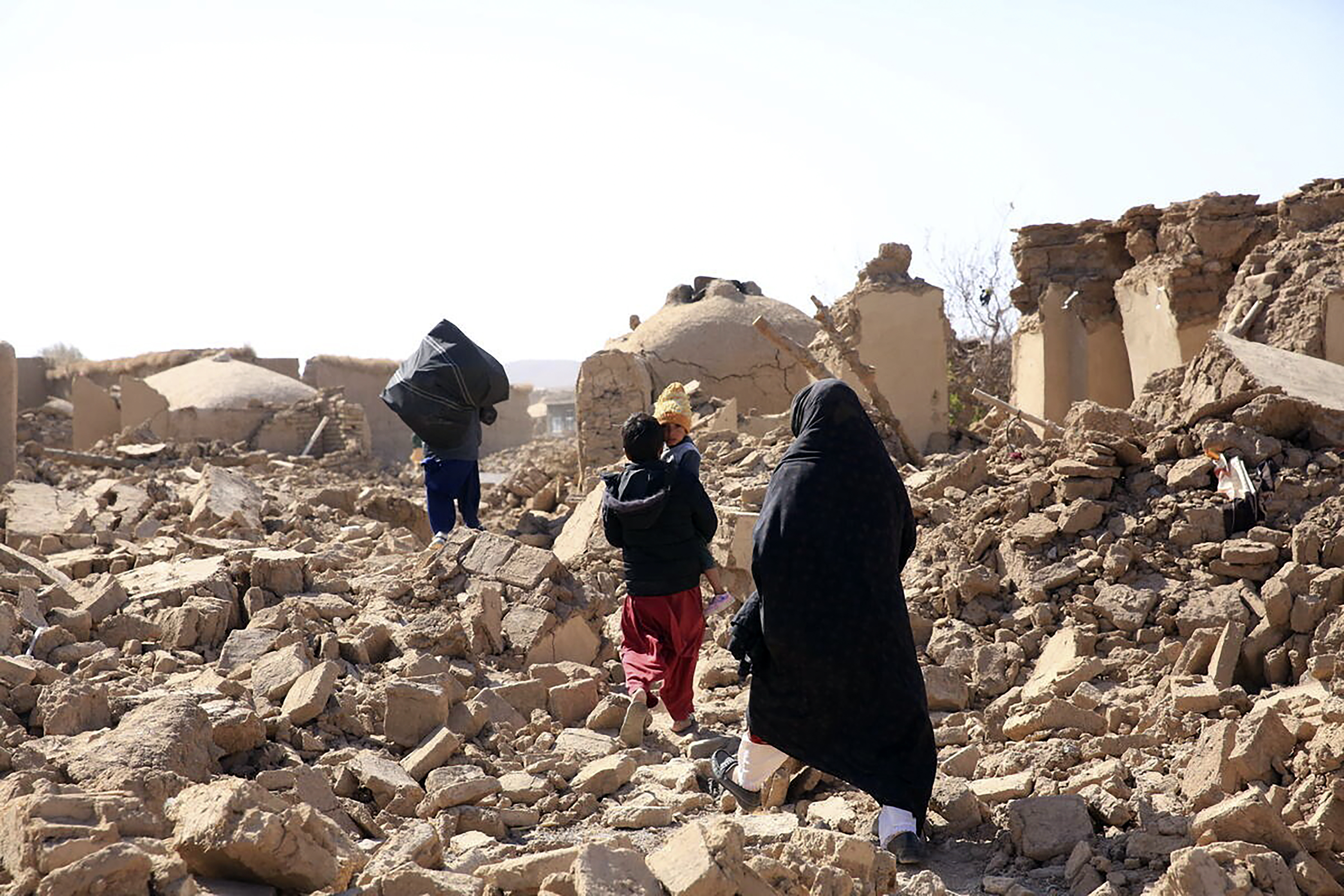 Mulher afegã caminha com os filhos em meio aos escombros após terremoto na província de Herat