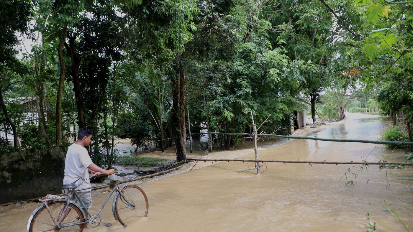 Morador atravessa área alagada com bicicleta em Teok, Assam