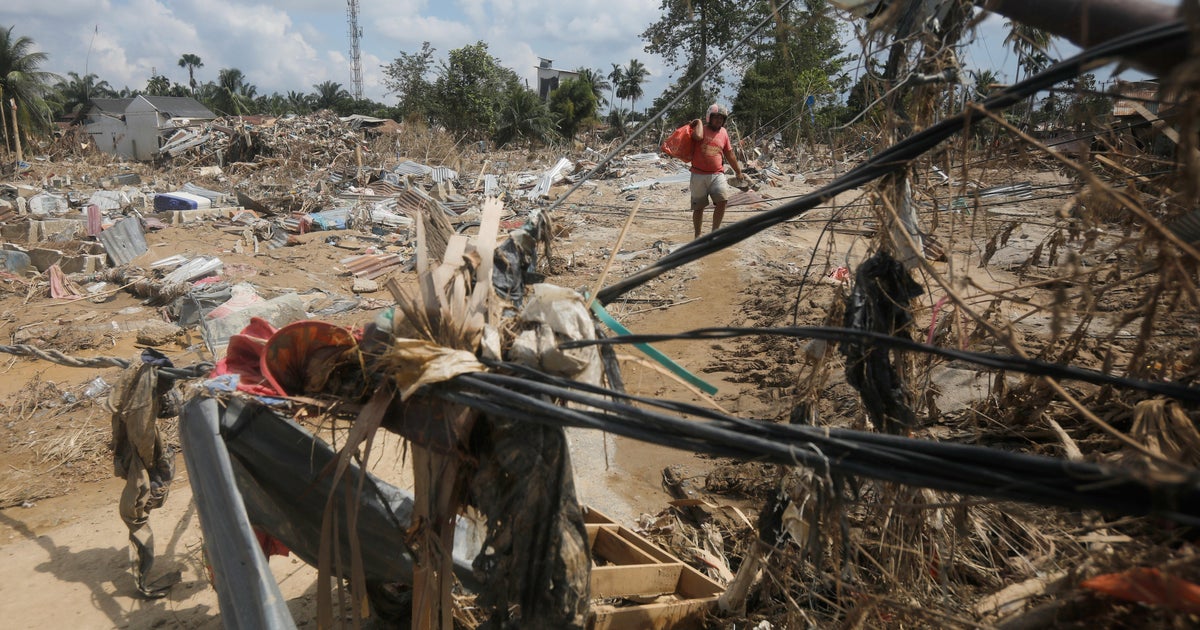 Sobrevivente carrega sacola de itens resgatados em área devastada por enchente repentina em Aceh Tamiang, Sumatra