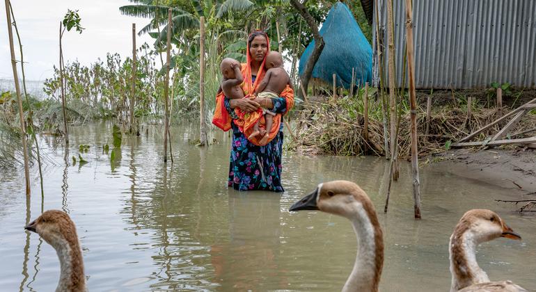 Mãe carrega as filhas gêmeas por águas de enchente durante a temporada de monções em Bangladesh