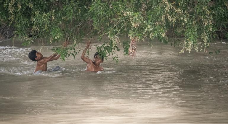 Crianças atravessam um canal alagado durante as enchentes de monção no Paquistão