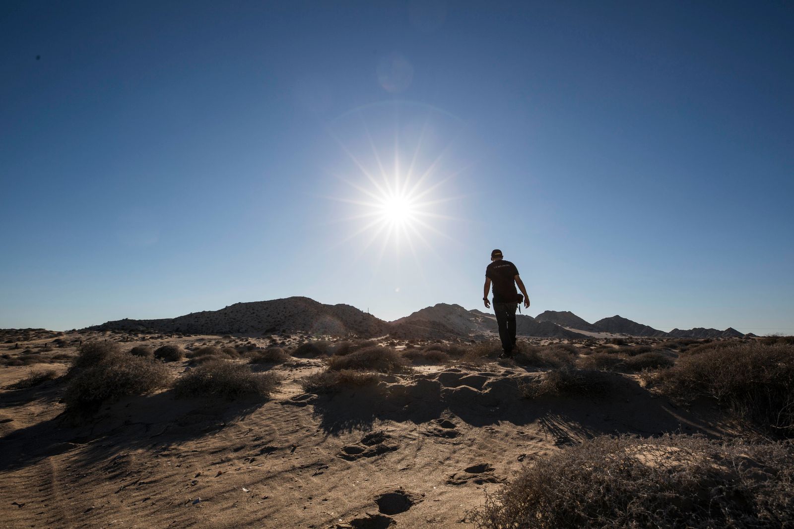Homem caminhando em paisagem desértica sob sol intenso