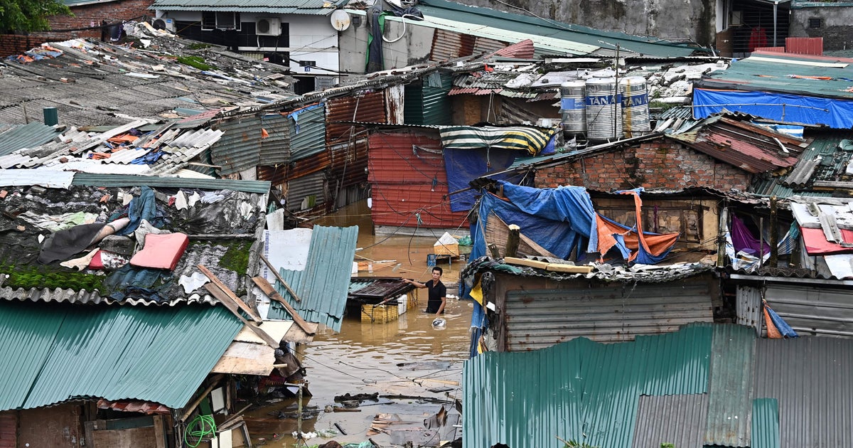 Homem atravessa águas de enchente por casas parcialmente submersas em Hanói, Vietnã, após o tufão Yagi